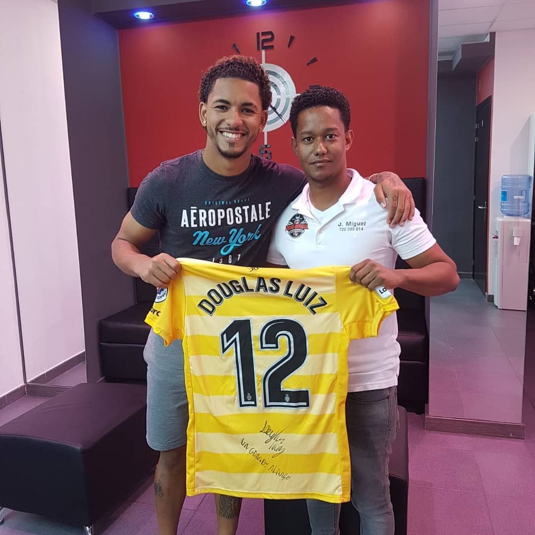 Dos hombres sostienen una camiseta amarilla de fútbol con la inscripción