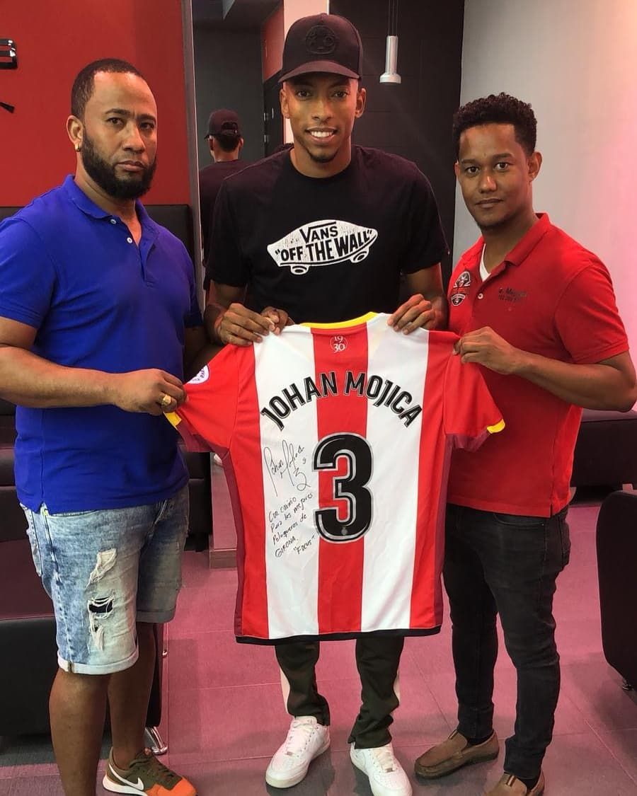 Tres hombres sostienen una camiseta de fútbol con el nombre