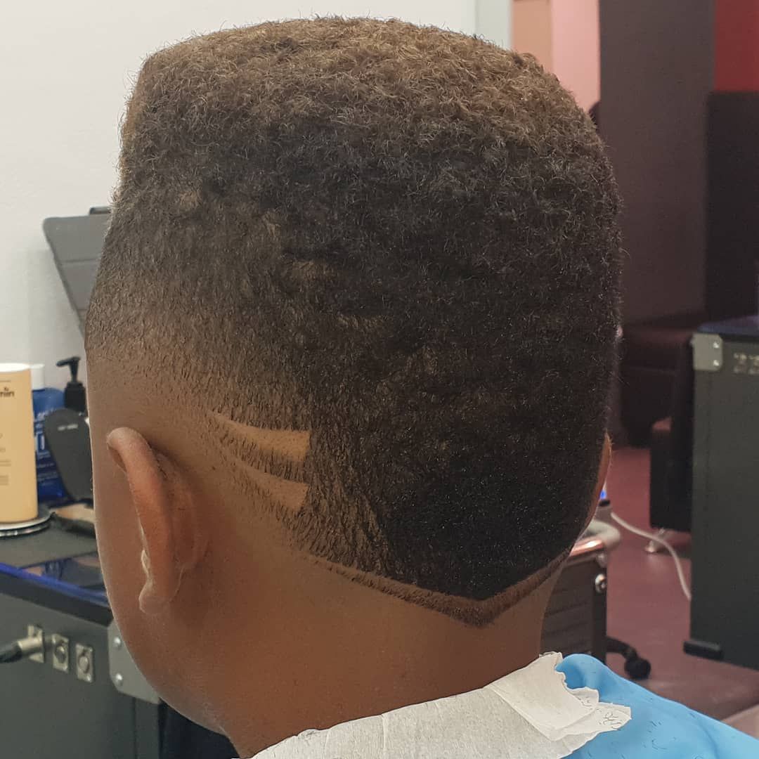 Persona con un corte de pelo corto que presenta un diseño recortado en la parte posterior de la cabeza; en interiores.