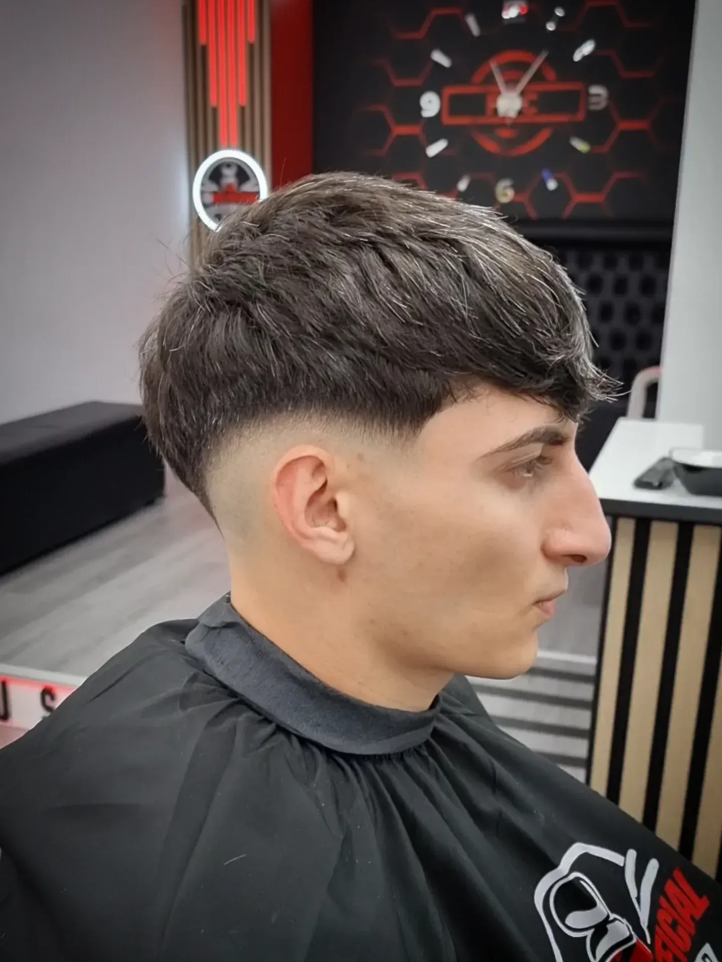 Hombre con un corte de pelo descolorido en una barbería, vistiendo una capa negra.