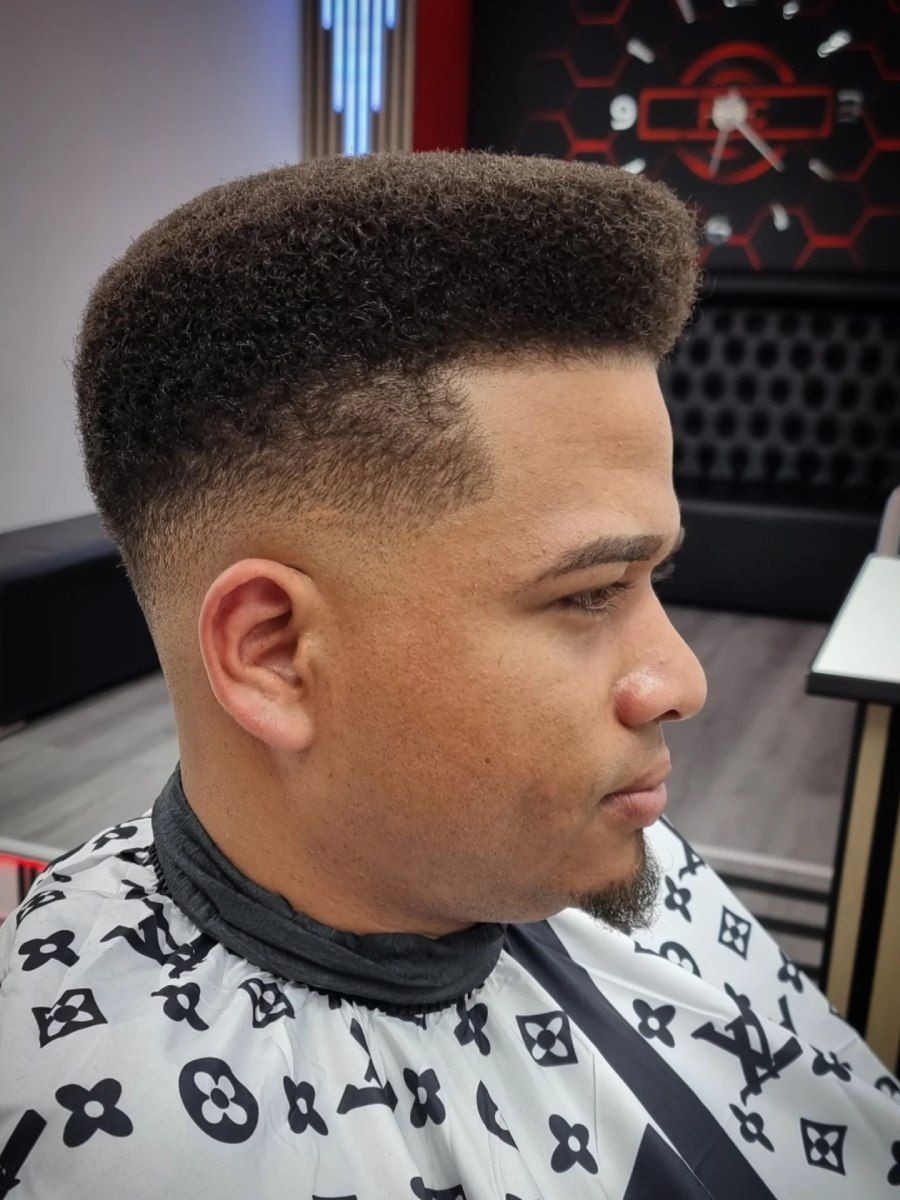 Hombre con corte de pelo alto, laterales descoloridos y vistiendo una capa de barbero.