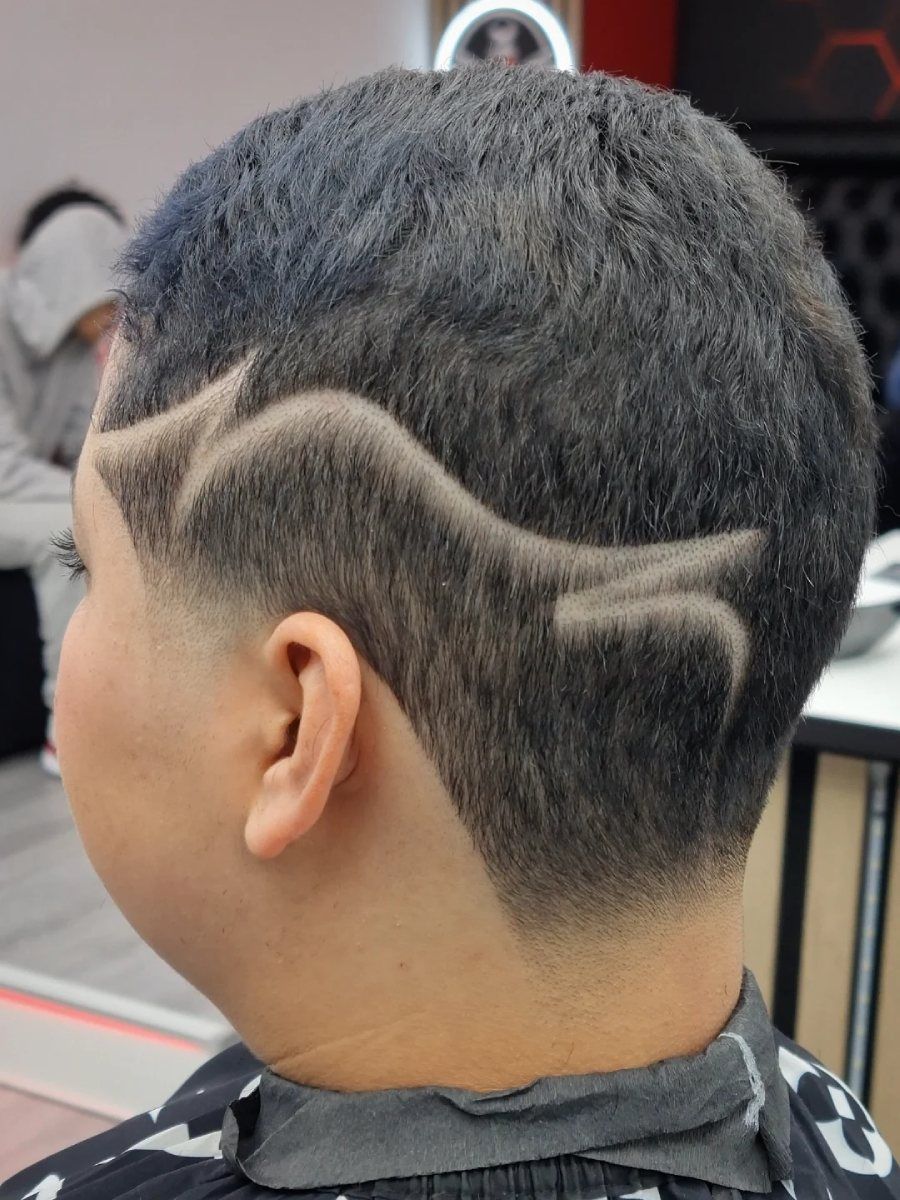 Persona con cabello corto y oscuro, con reflejos azules. Su corte presenta un diseño rapado a un lado y la nuca descolorida.