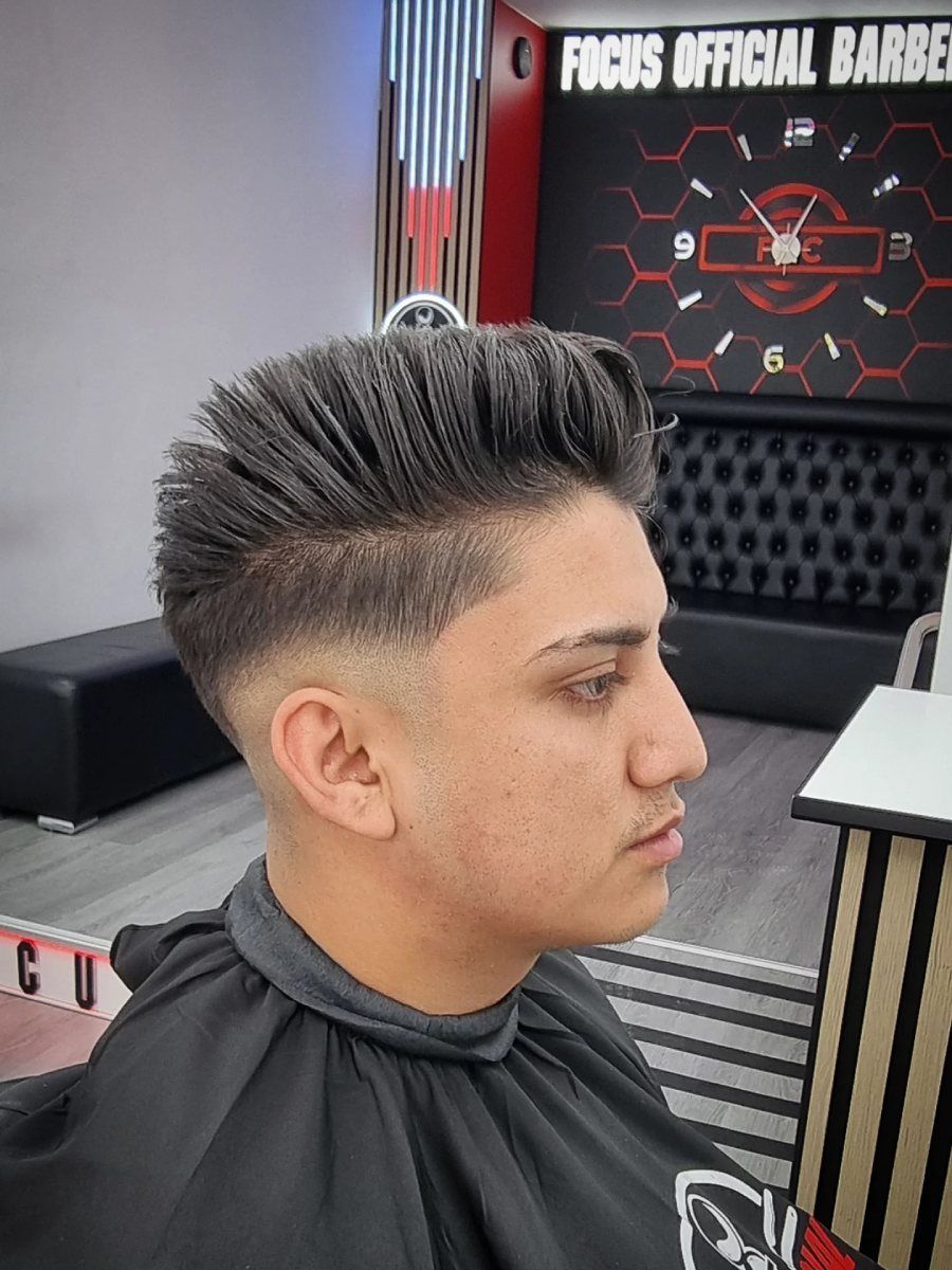 Hombre con un corte de pelo descolorido en una barbería, vestido con una capa.