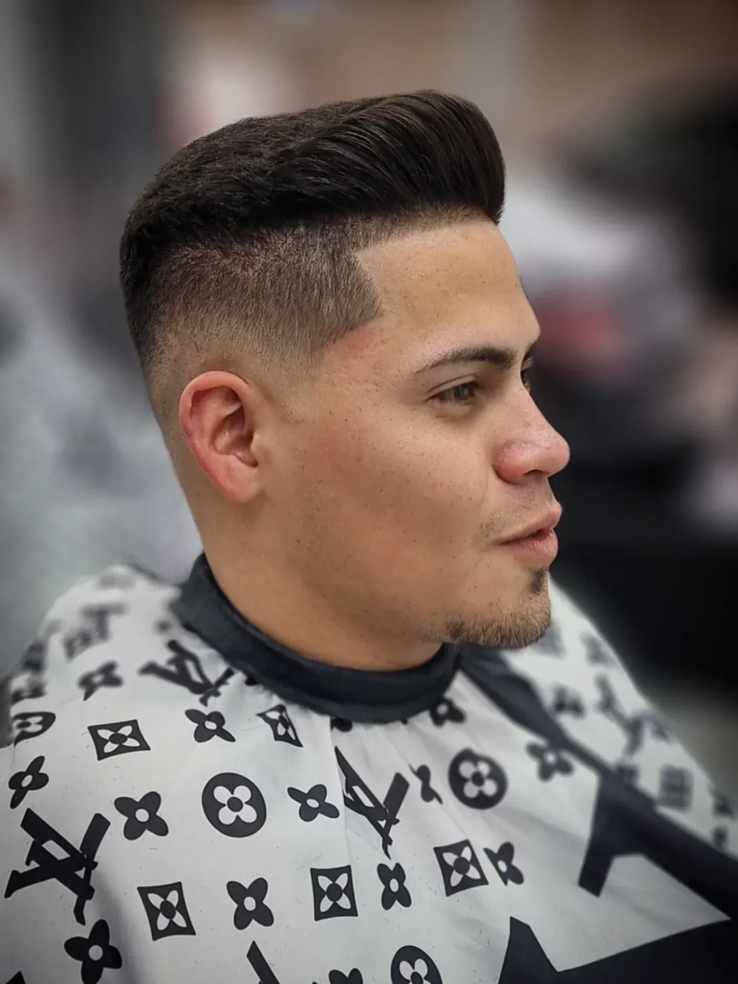 Hombre con un corte de pelo descolorido, vistiendo una capa de barbero con estampado blanco y negro.