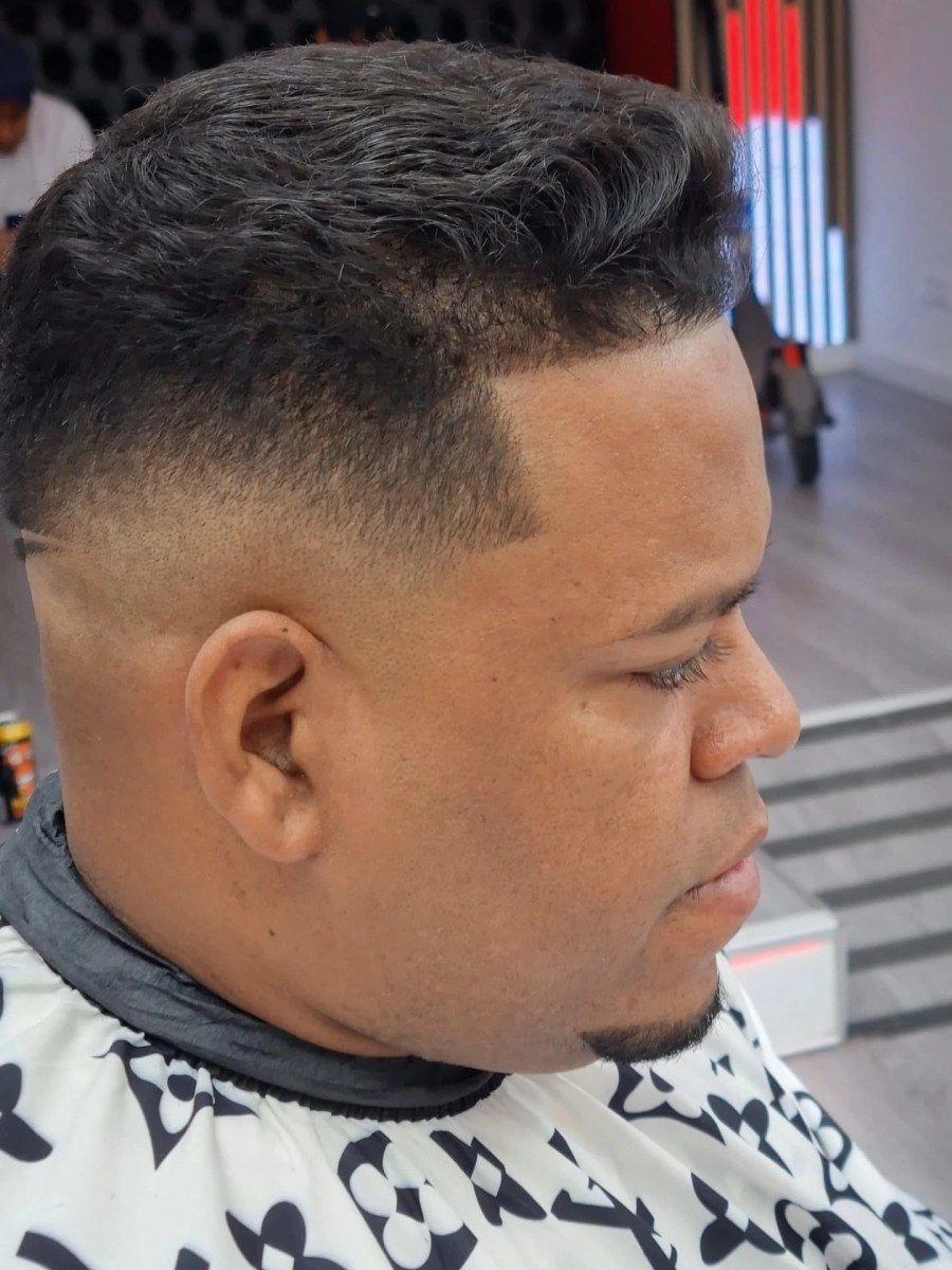 Hombre con un corte de pelo descolorido en una barbería, vistiendo una capa de corte de pelo, mirando hacia un lado.