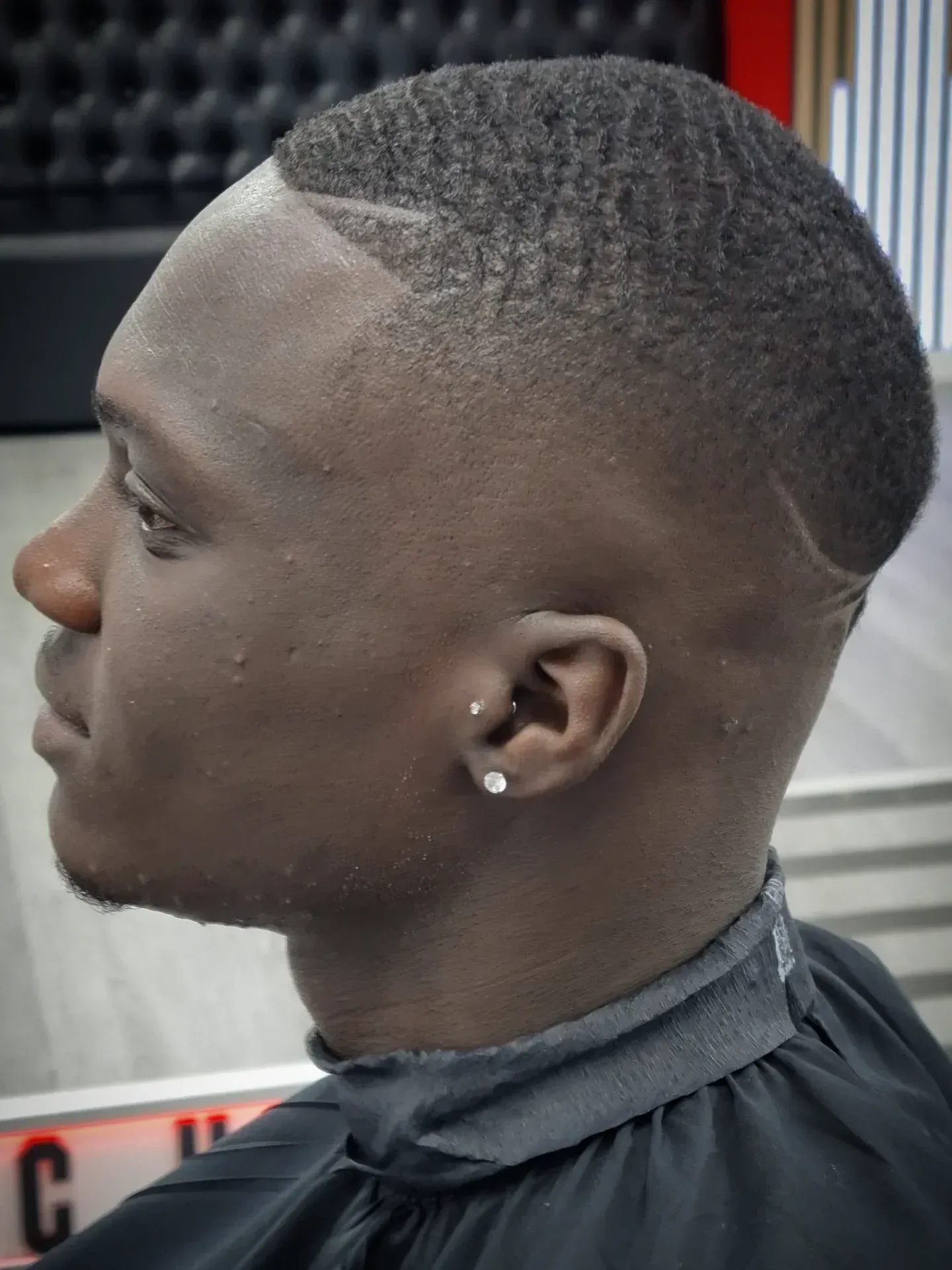 Primer plano de una persona con cabello oscuro, corto y ondulado, con un corte de pelo desvanecido y vestida con una bata negra.