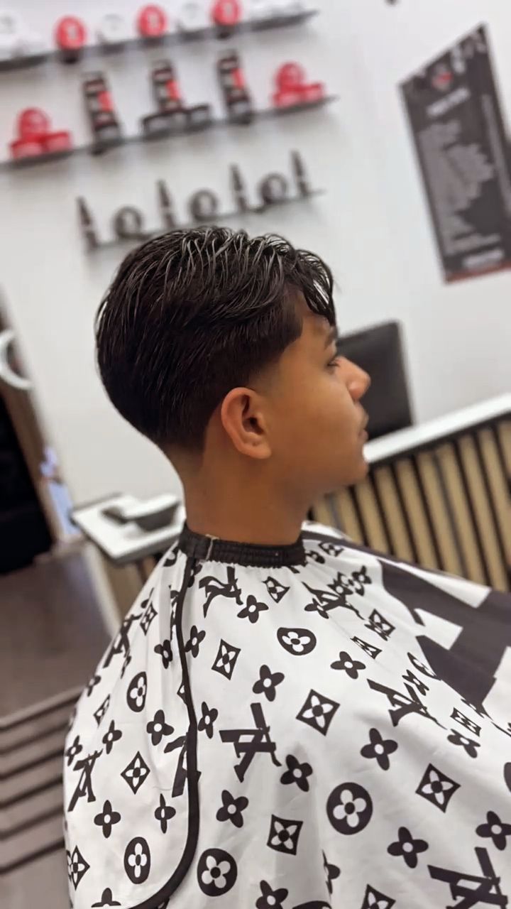 Persona joven con un corte de pelo en una barbería, vistiendo una capa blanca con dibujos negros.