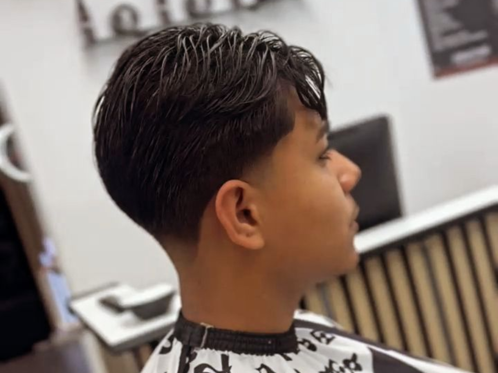 Chico con el pelo descolorido en una barbería. De perfil, lleva el pelo oscuro peinado hacia atrás y los laterales muy cortos.