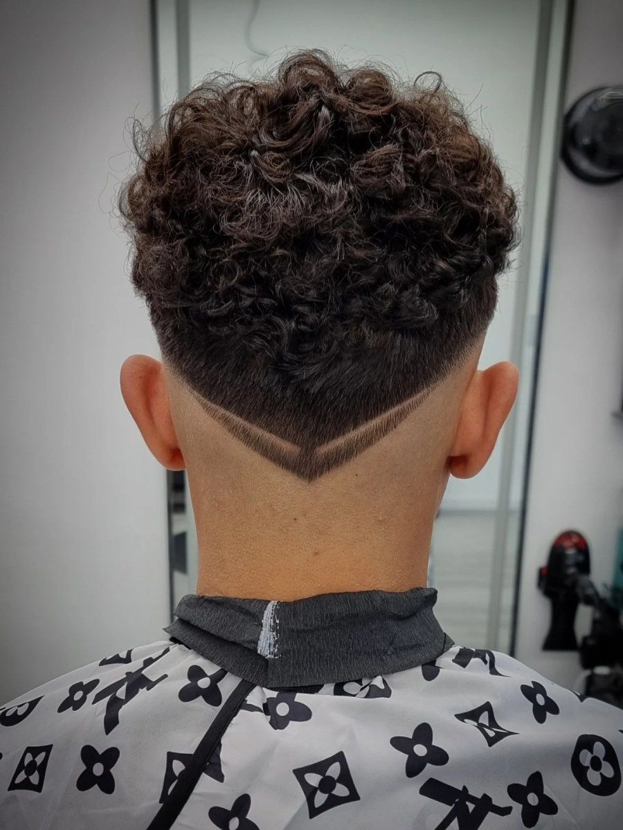 Parte posterior de la cabeza de una persona con cabello castaño rizado. Un corte de pelo cónico con un diseño oscuro en forma de V en la nuca.