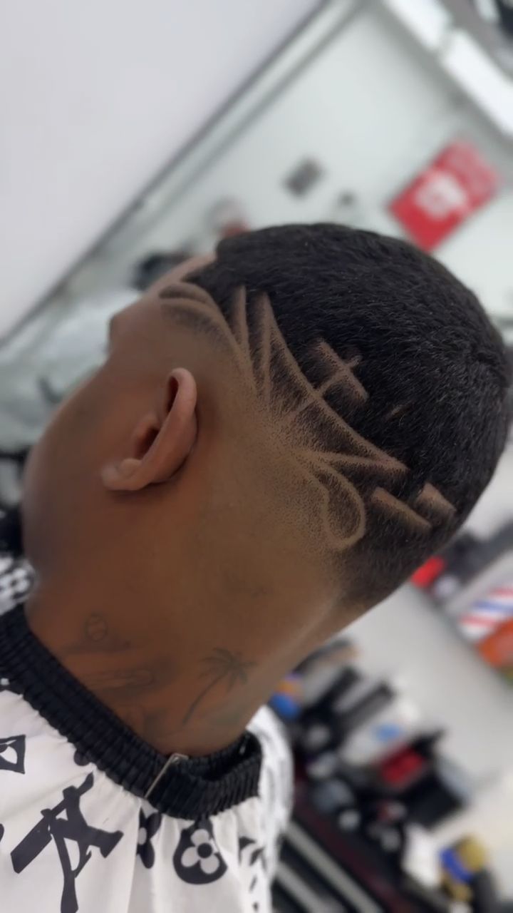 Primer plano de la cabeza de una persona con un corte de pelo estampado y un tatuaje en el cuello, vestida con una capa de barbero.