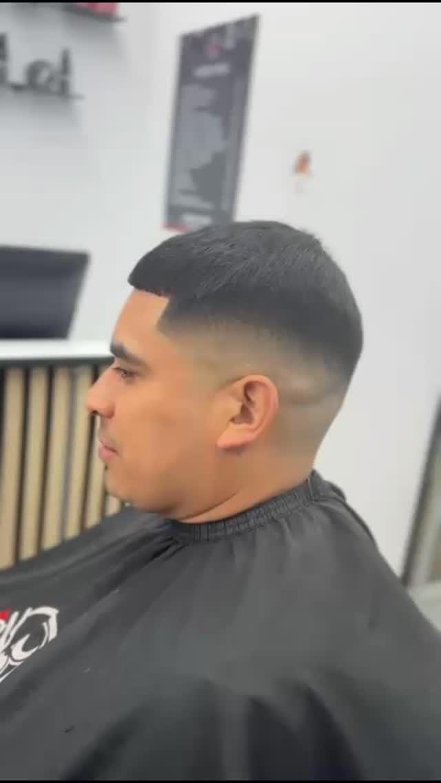 Hombre con un corte de pelo descolorido en una barbería, vistiendo una capa de barbero negra.