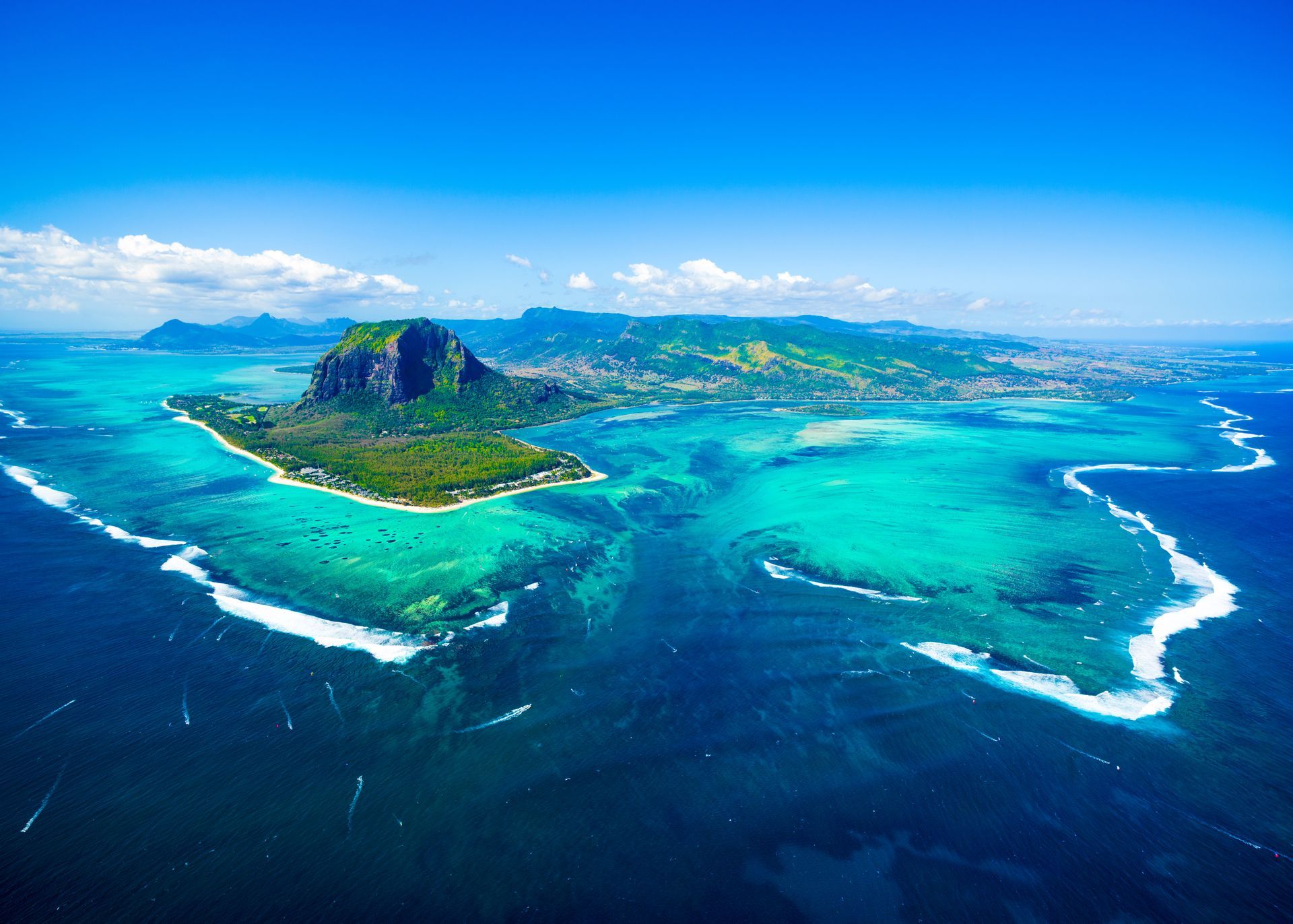 Vue aérienne d'une île tropicale aux lagons turquoise, aux vagues écumeuses et au sommet d'un volcan verdoyant