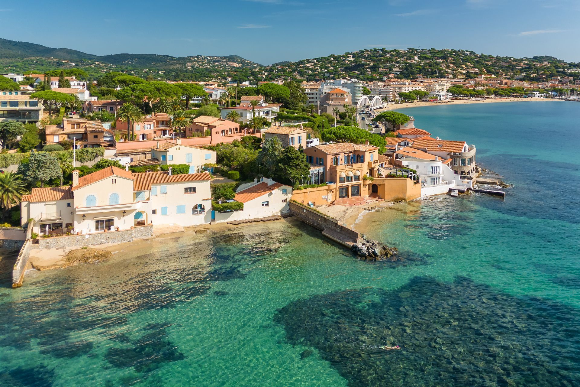 Village balnéaire coloré avec une eau turquoise, un rivage rocheux et des maisons sur une colline côtière ensoleillée