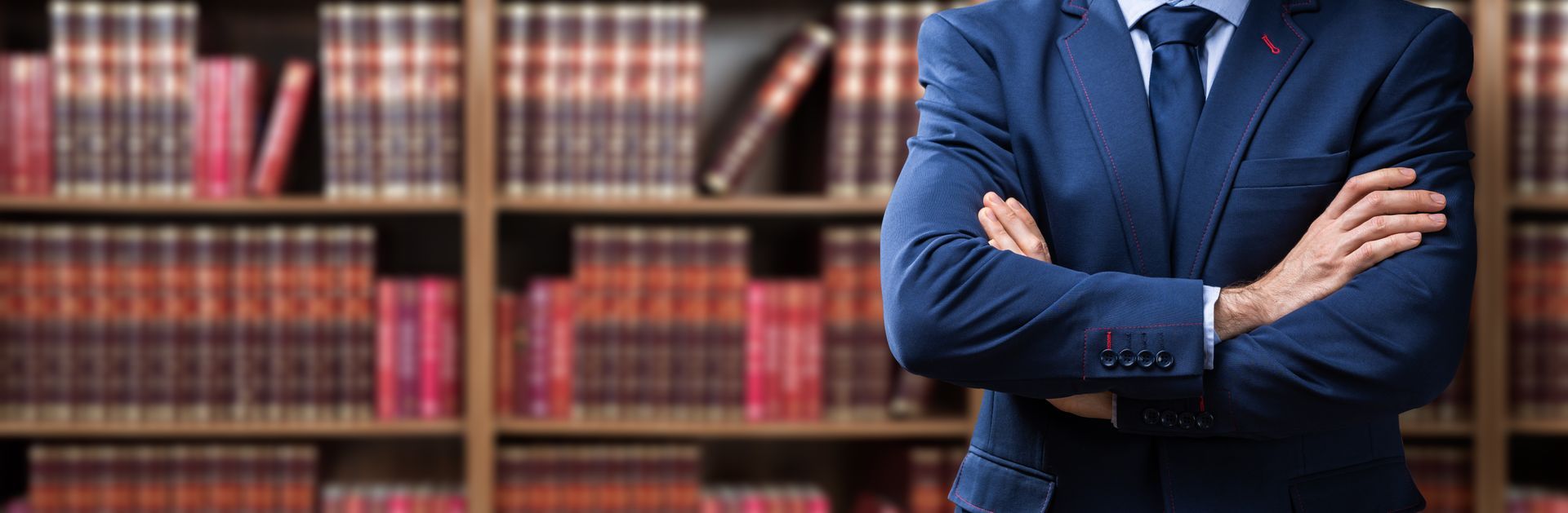 Une personne en costume, les bras croisés, se tient devant un mur de livres de droit dans une bibliothèque.