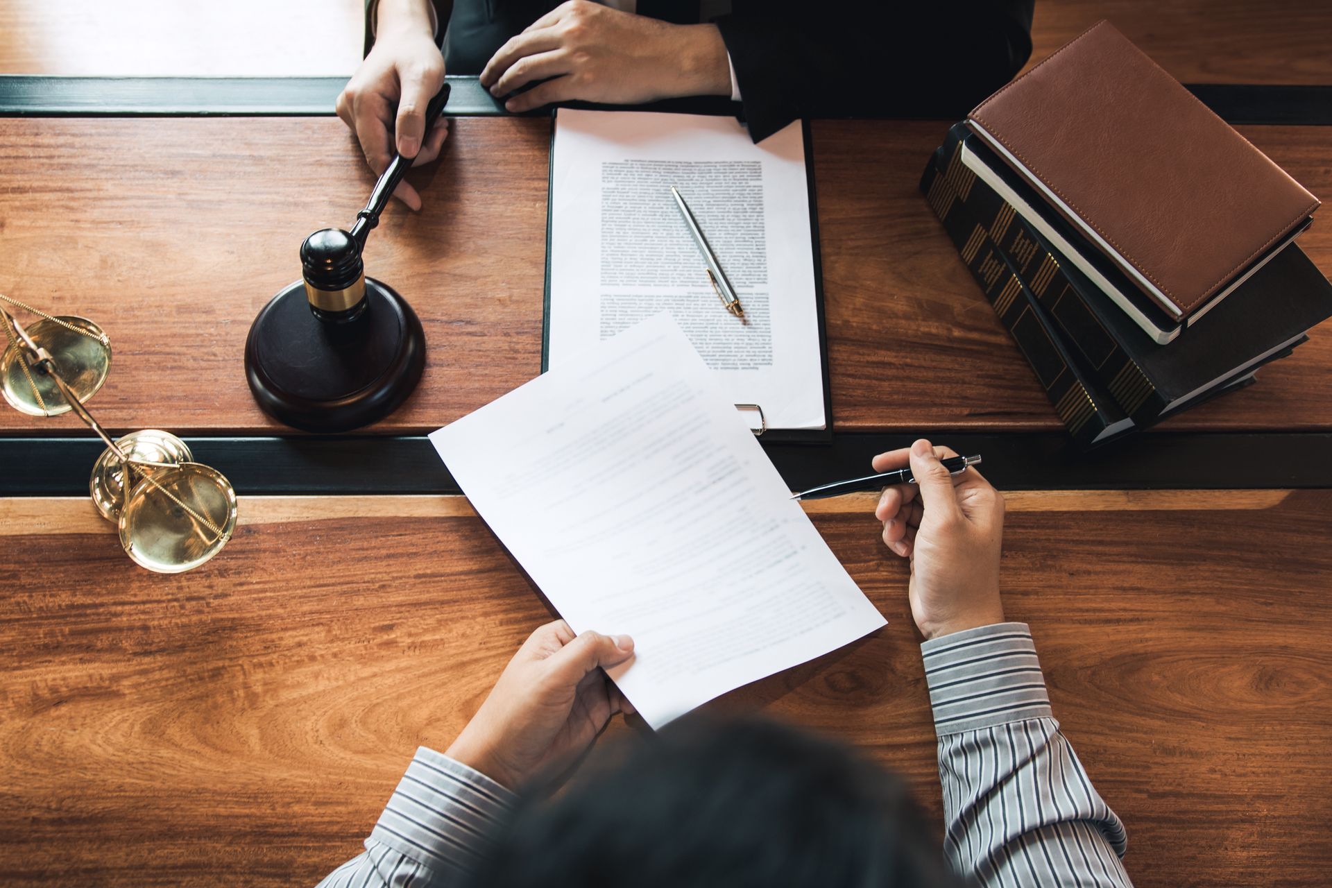 Des personnes signent un document juridique autour d'une table de conférence en bois, un maillet et des livres à proximité.