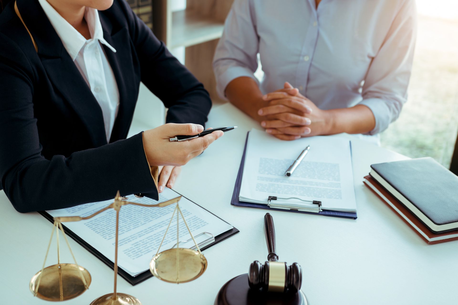 Deux professionnels, dans un bureau lumineux, discutent de documents, un stylo posé sur un bureau où se trouvent un ordinateur portable et une balance de la justice.