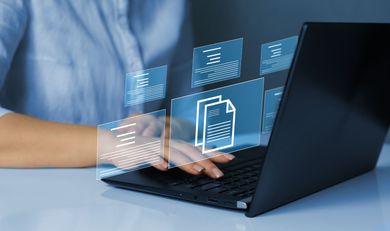 Des mains tapent sur un ordinateur portable avec des icônes de fichiers numériques lumineuses flottant au-dessus du clavier.
