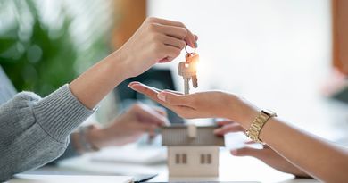 Des mains échangent des clés de maison au-dessus d'une maquette de maison dans un bureau lumineux.
