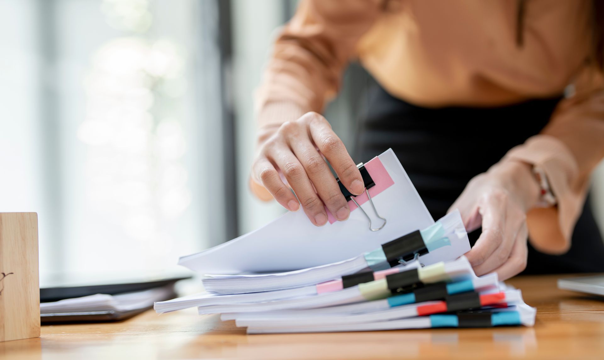 Des mains trient des échantillons de papier coloré sur un bureau où sont empilées des feuilles et des marqueurs.