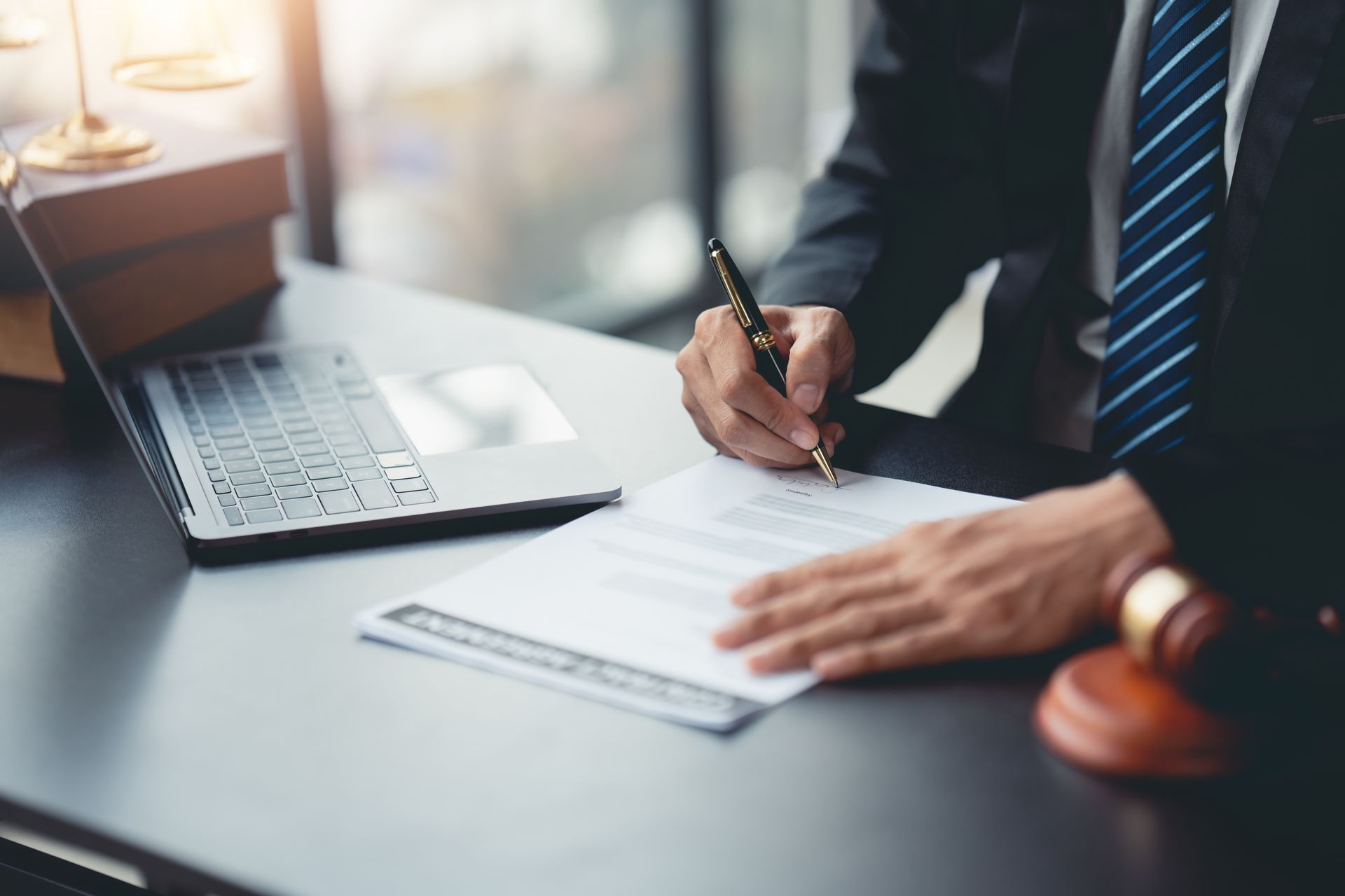 Un homme d'affaires signe un document à côté d'un ordinateur portable et d'un maillet posés sur un bureau.