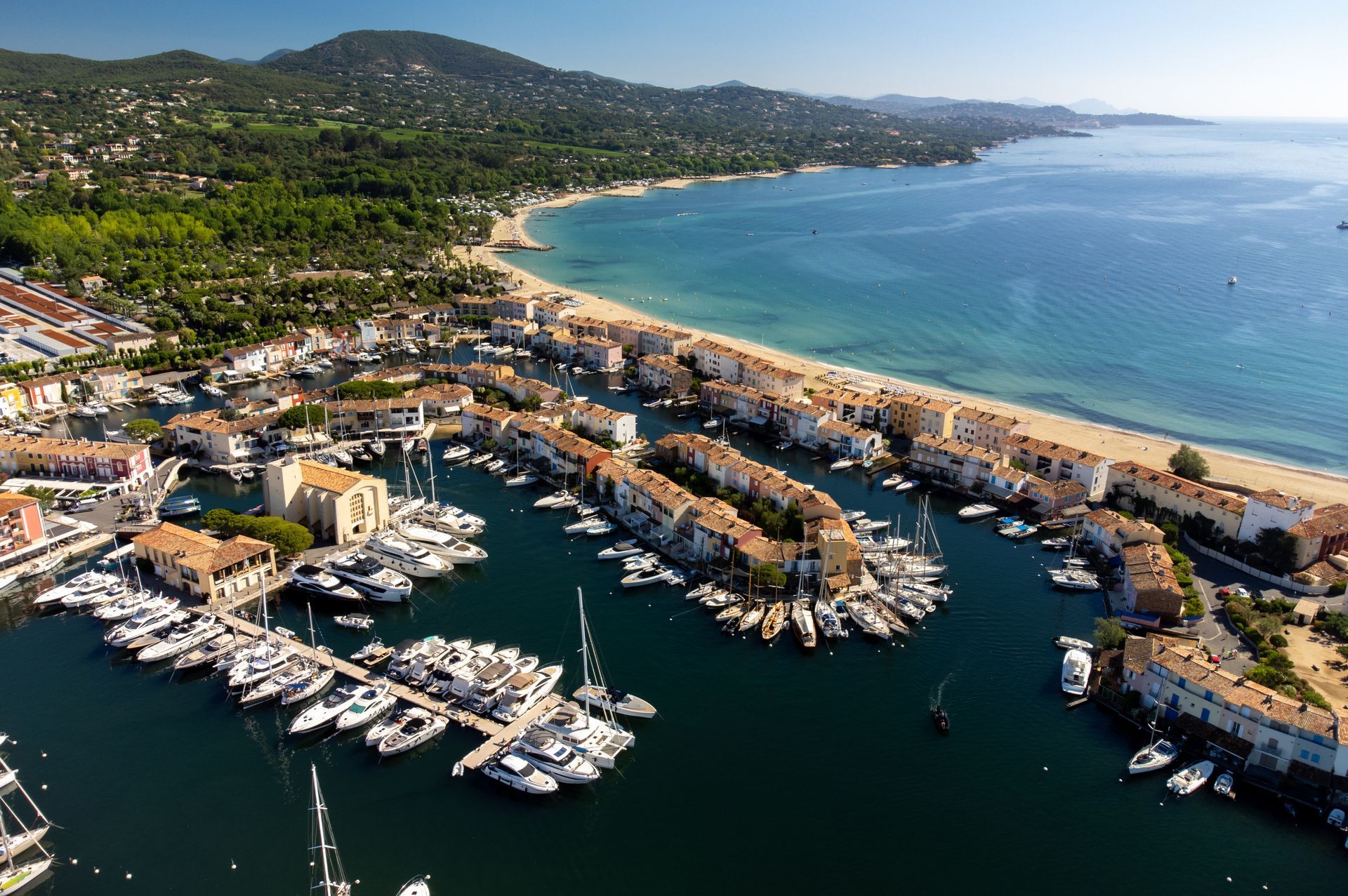 Vue aérienne d'un port de plaisance avec des yachts blancs près d'une ville côtière et d'une plage donnant sur une baie bleue