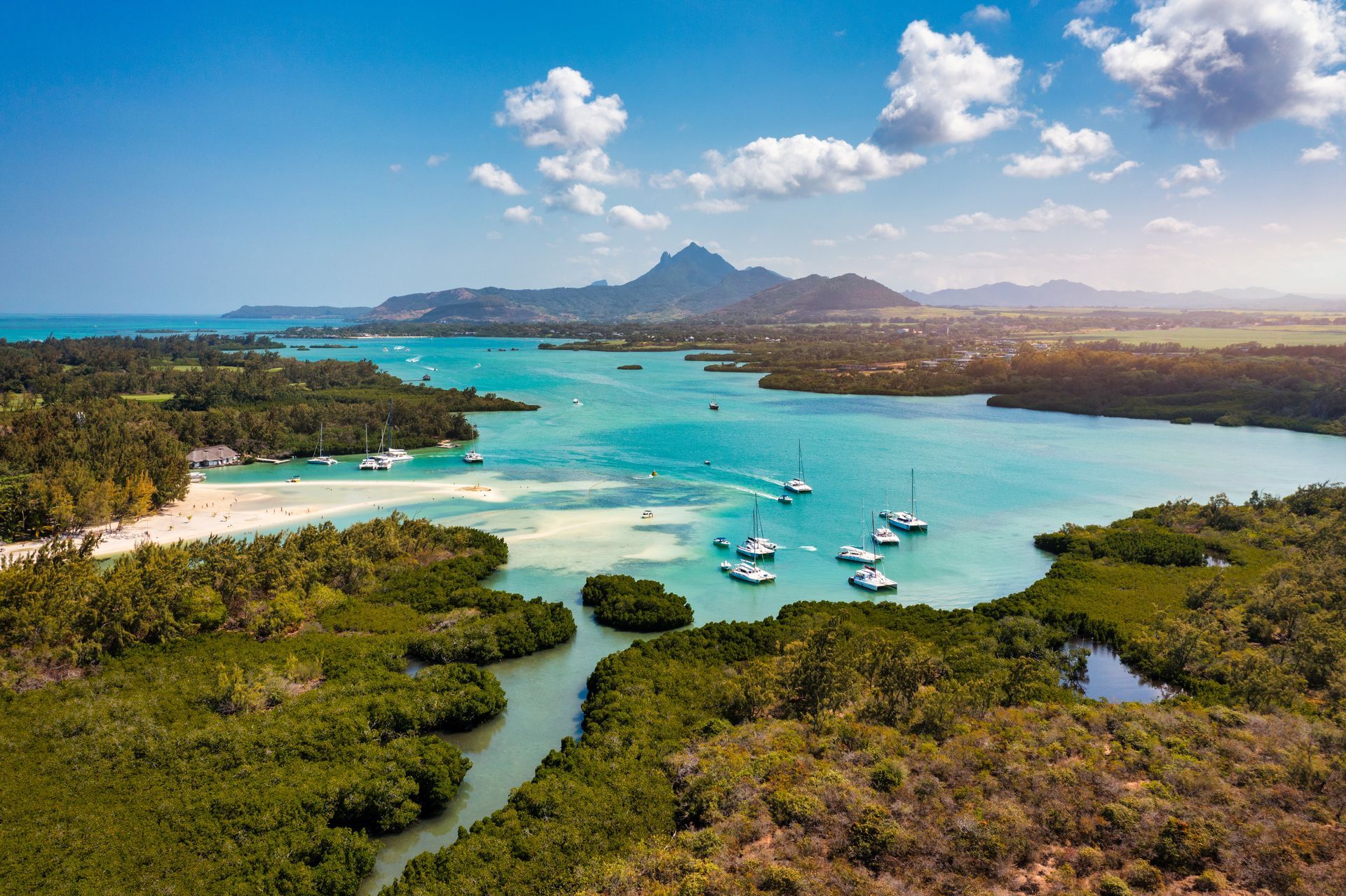 Lagon turquoise avec bateaux, végétation, rivage sablonneux et montagnes au loin sous un ciel bleu