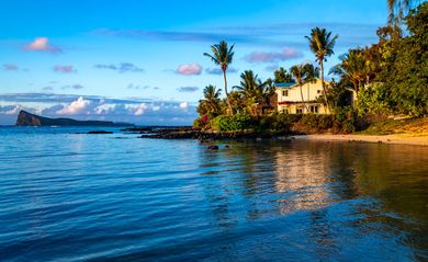 Littoral tropical aux eaux bleues et calmes, palmiers et une maison côtière ensoleillée en bord de plage