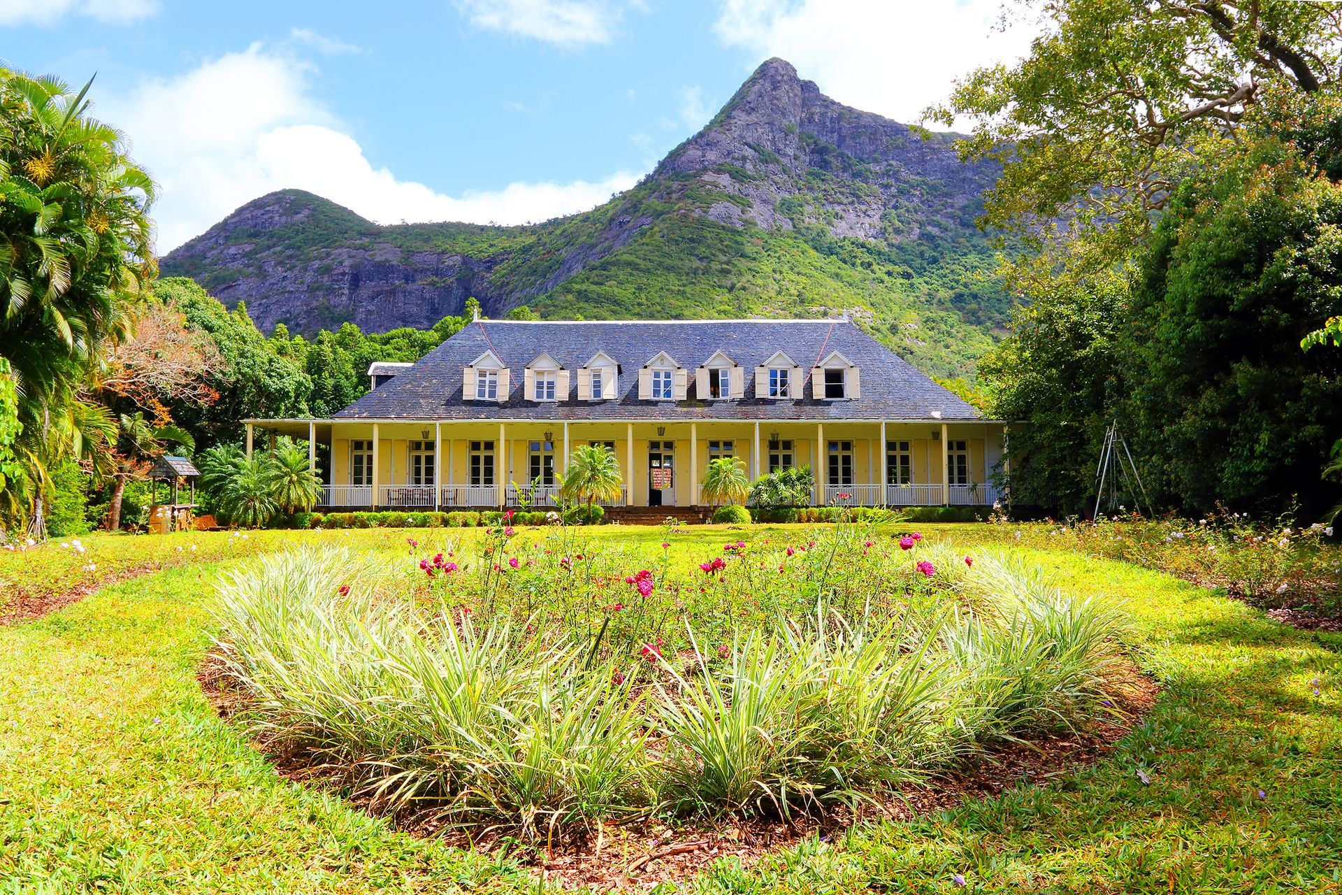 Grande maison avec un jardin soigné et une vue sur les montagnes sous un soleil éclatant