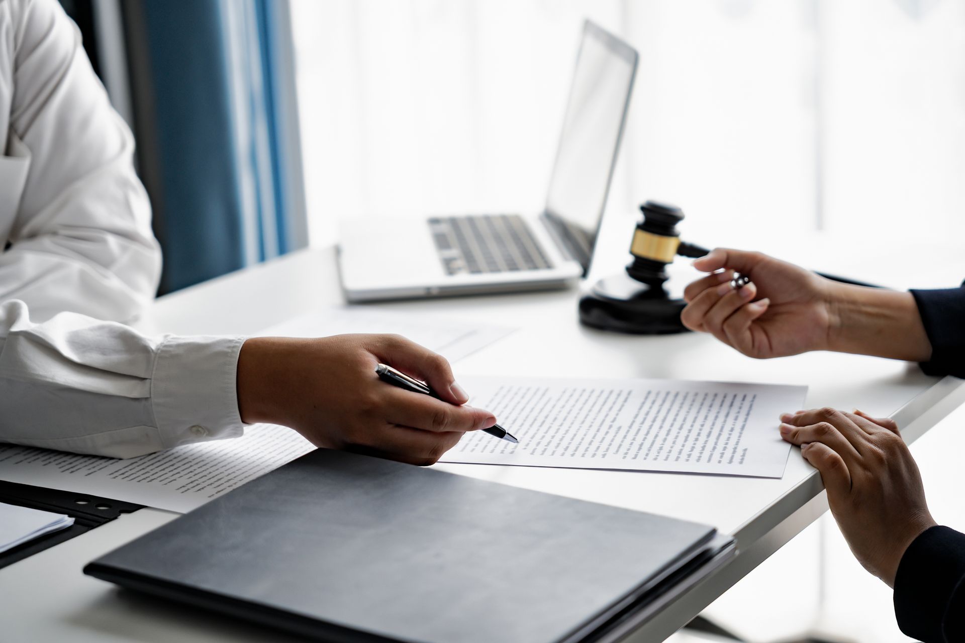 Deux personnes assises à un bureau examinent des documents avec un ordinateur portable et un marteau à proximité.