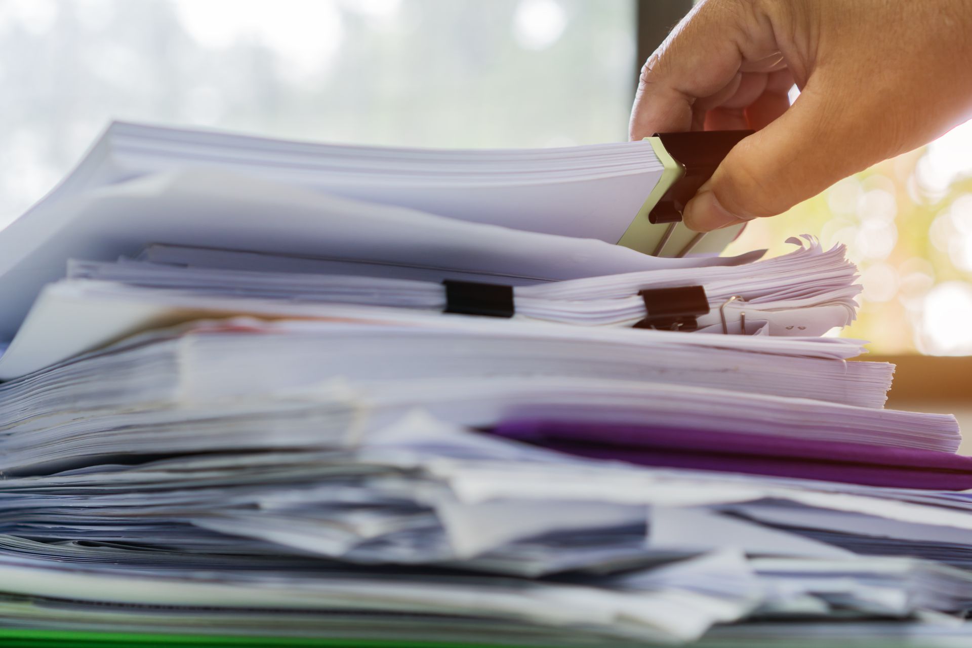 La main d'une personne trie une pile de papiers maintenus ensemble par des trombones.