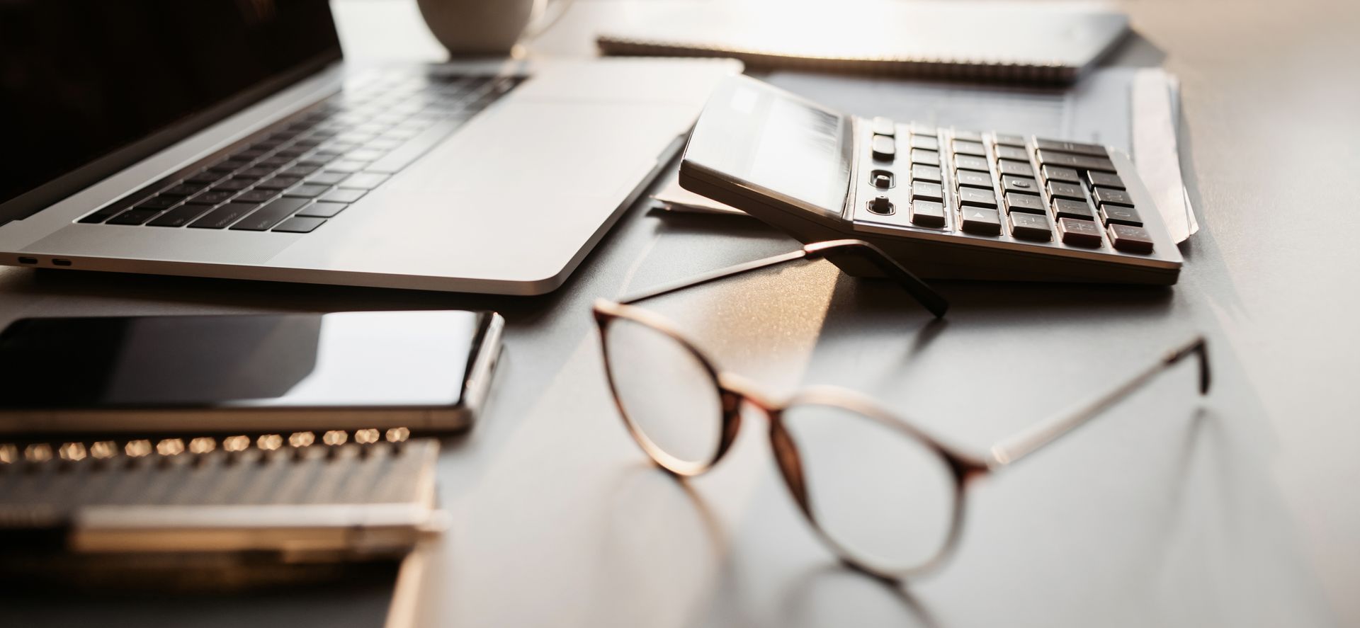 Ordinateur portable, lunettes, téléphone et bloc-notes sur un bureau, suggérant du travail ou des études.