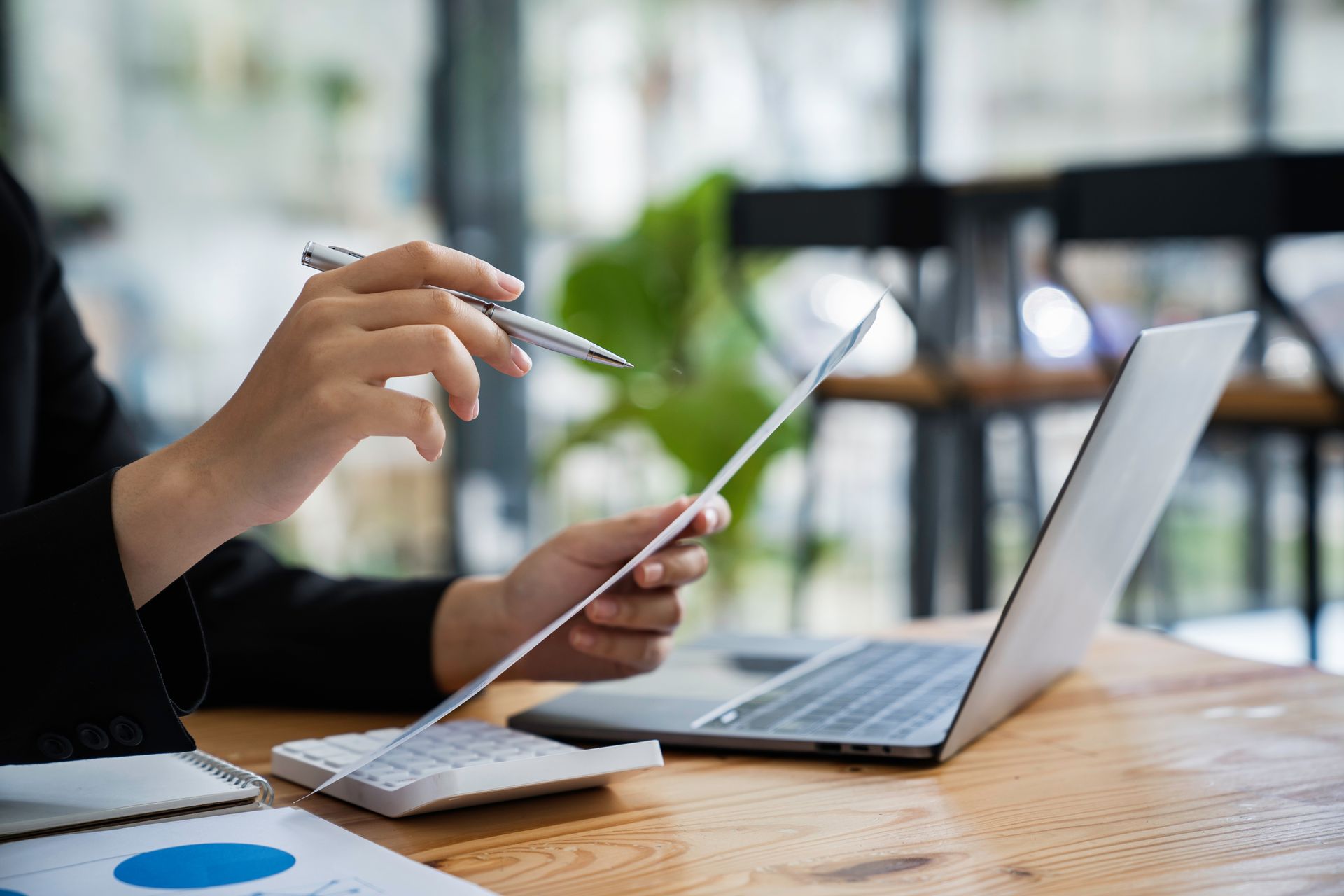 Personne travaillant sur un ordinateur portable, tenant un stylo et du papier, avec une calculatrice sur le bureau.