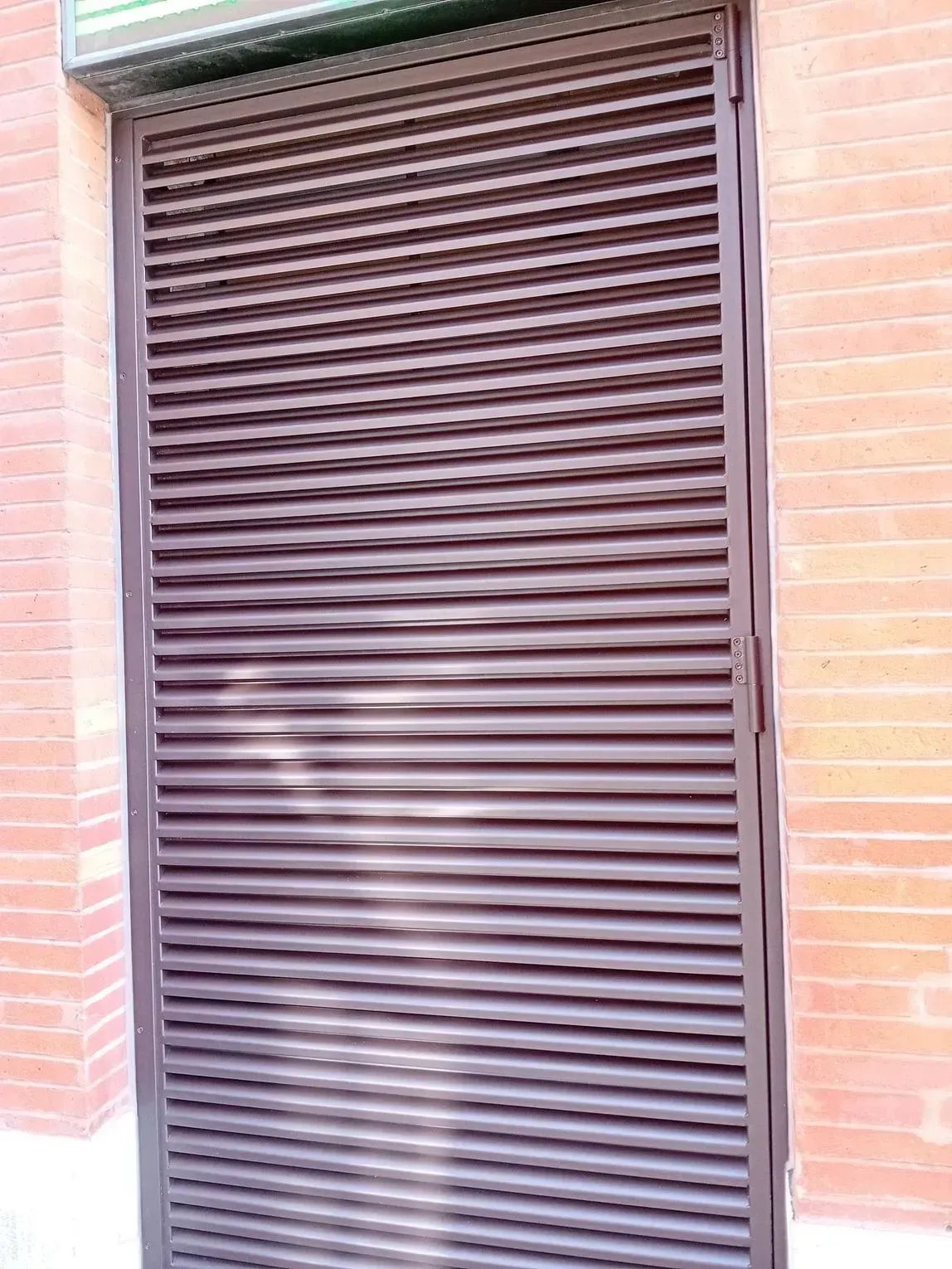 Volet roulant métallique marron dans une porte en briques