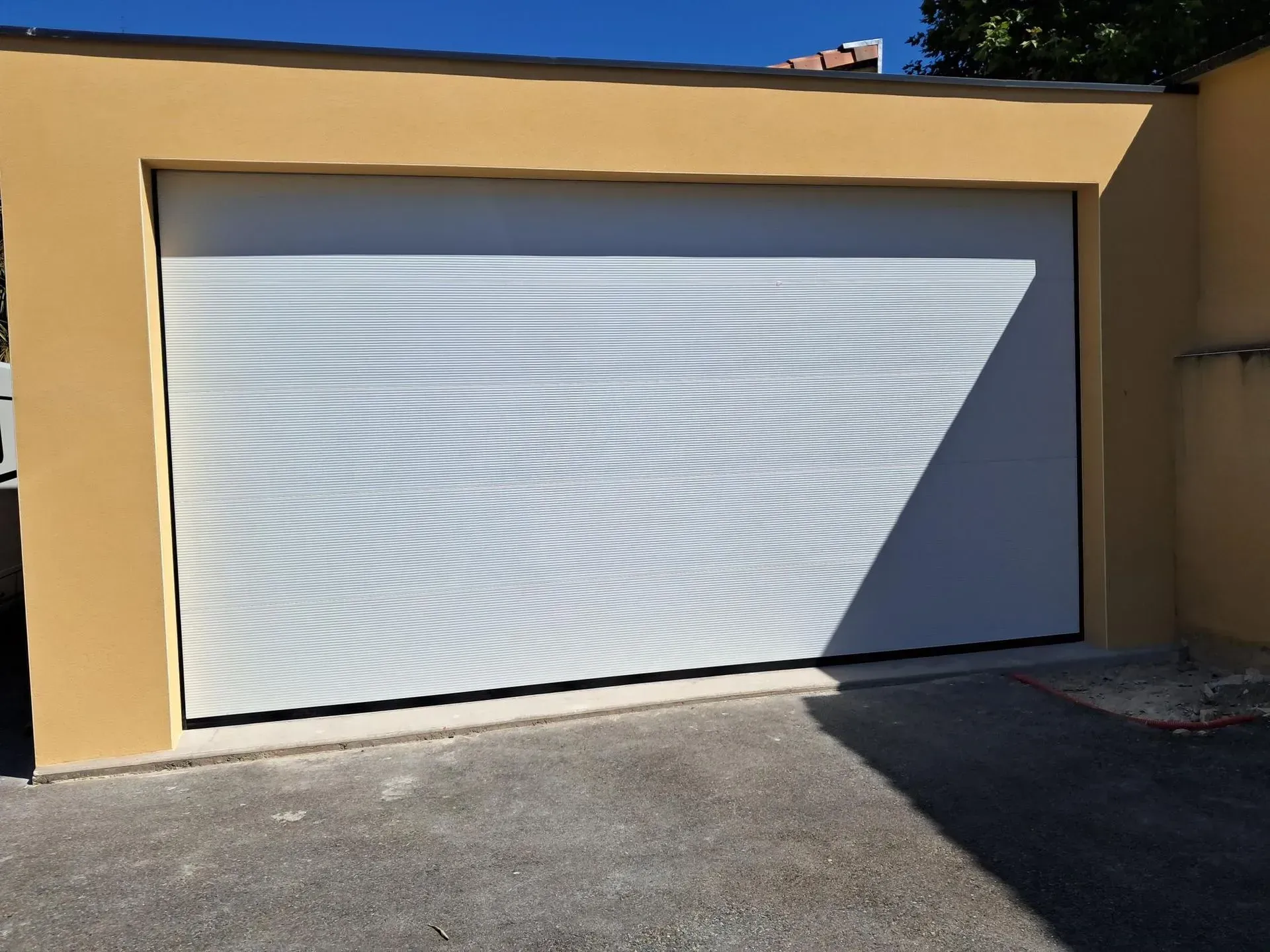 Porte de garage blanche sur un bâtiment beige où le soleil projette des ombres rayées