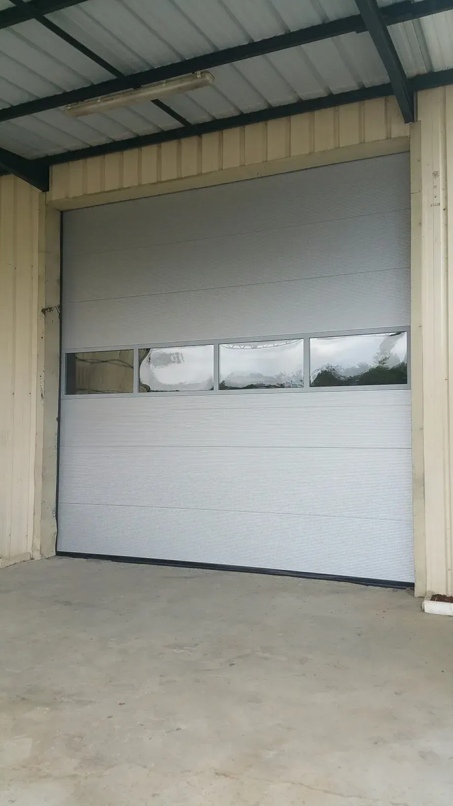 Porte de garage sectionnelle blanche fermée dans une travée d'un bâtiment industriel beige