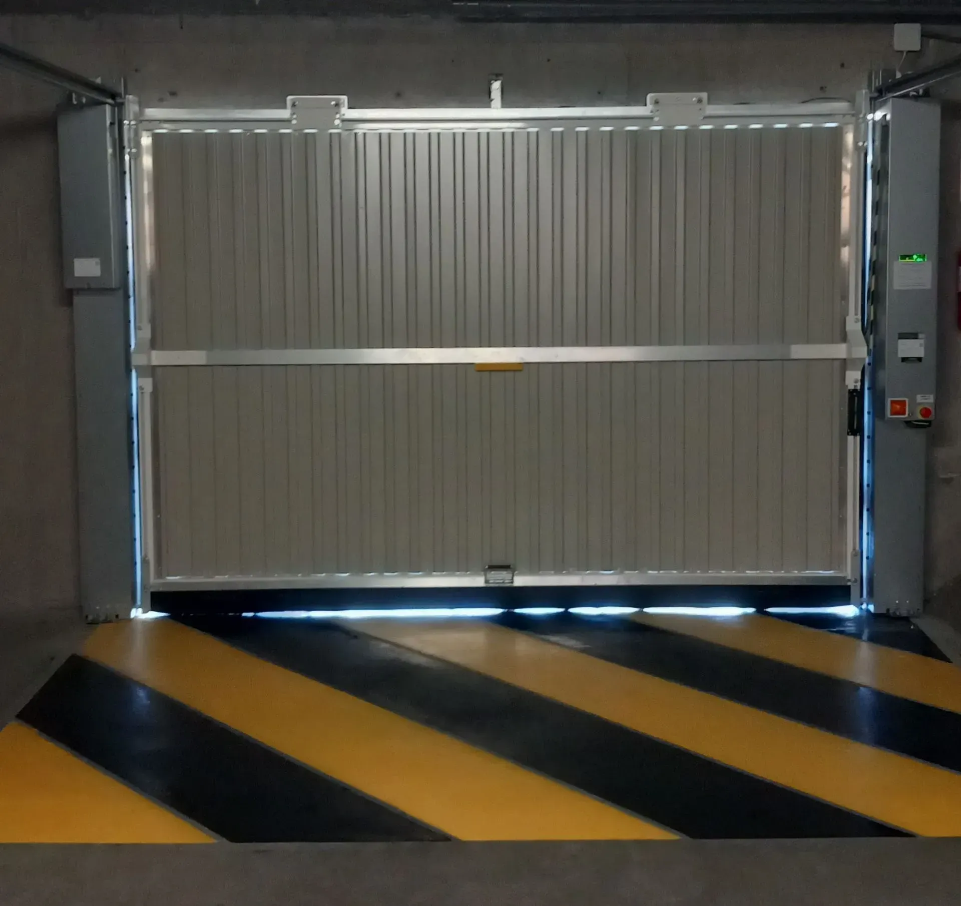 Porte de garage industrielle fermée avec bandes de sol noires et jaunes et panneau de commande mural