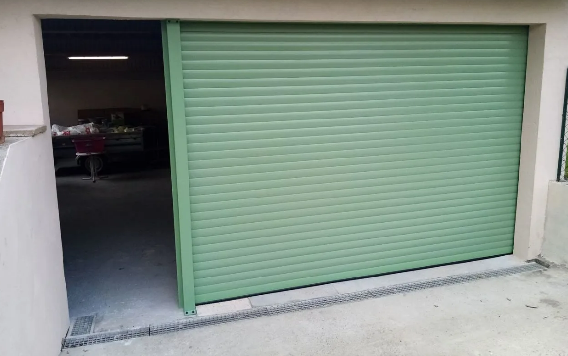 Porte de garage enroulable verte partiellement ouverte sur un espace de travail intérieur sombre
