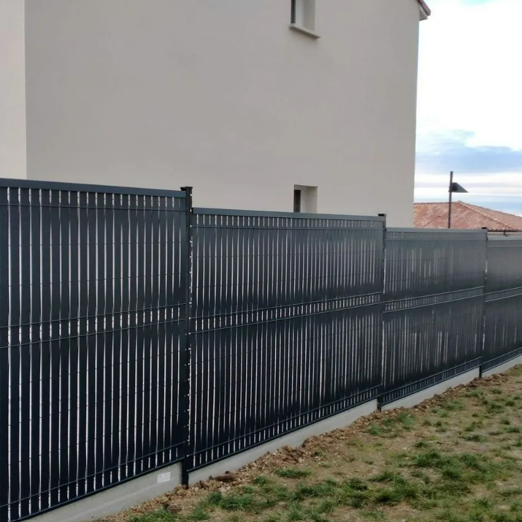 Clôture en métal noir à côté d'un bâtiment beige et d'une cour herbeuse sous un ciel couvert