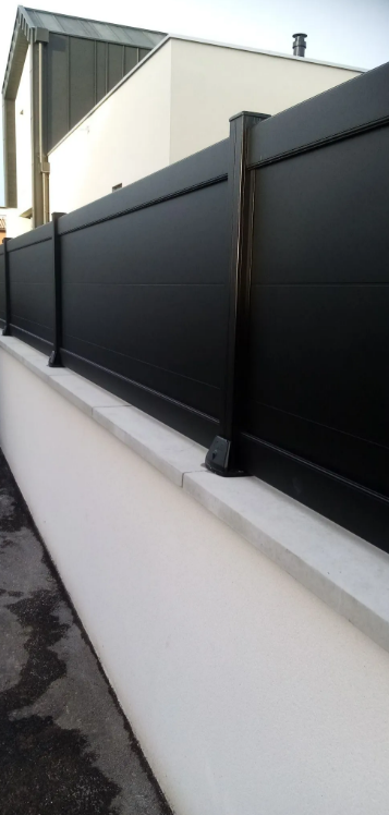 Clôture métallique noire le long d'un mur blanc, à côté d'un bâtiment et d'un trottoir extérieur.