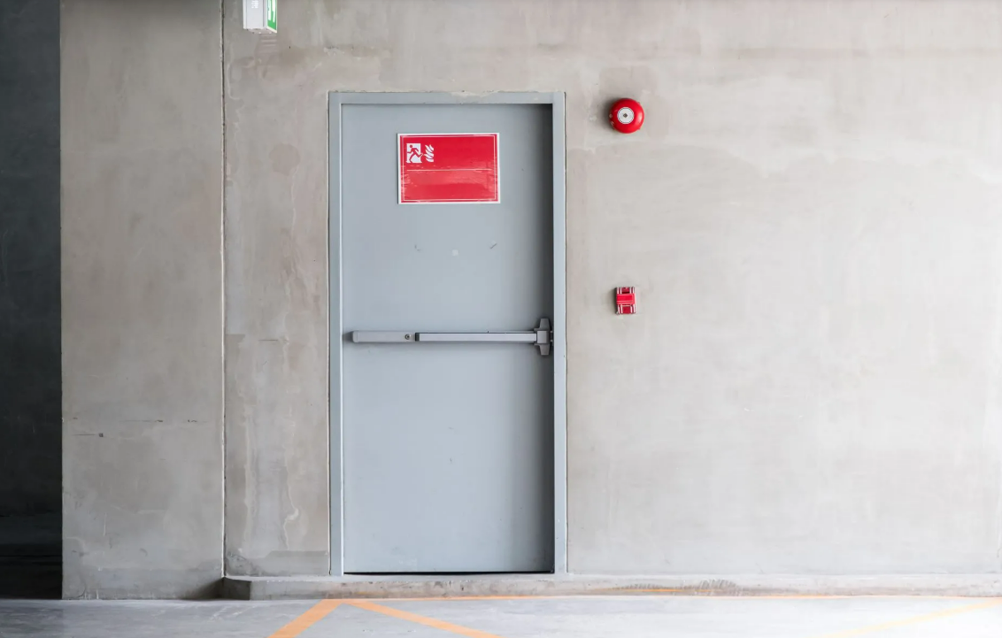 Porte métallique grise avec panneau rouge et boutons d'urgence sur un mur en béton