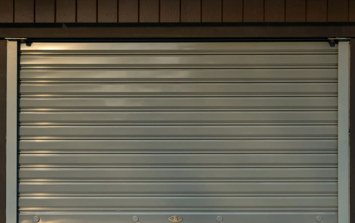 Porte de garage sectionnelle en métal gris fermé, avec lames horizontales et cadre mural marron.