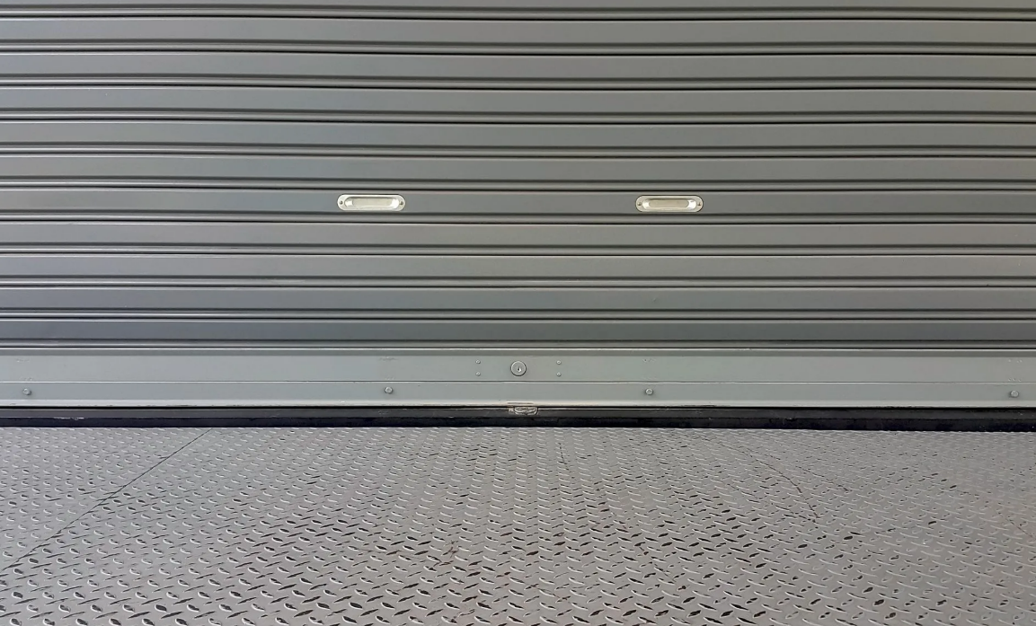 Porte de garage métallique grise fermée au-dessus d'un sol en béton texturé.