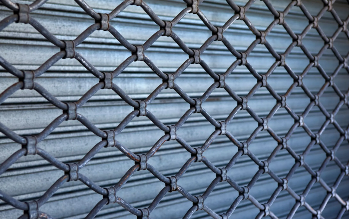Gros plan sur une clôture en grillage métallique devant un mur en tôle ondulée