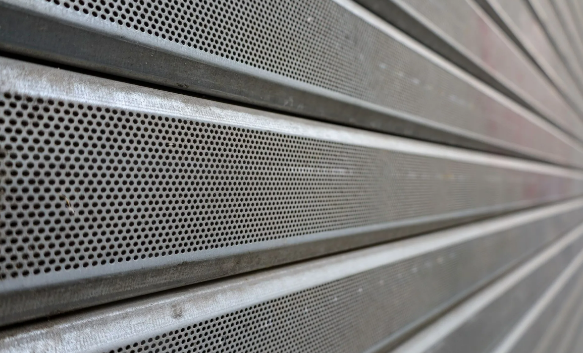 Gros plan sur un bardage métallique perforé à lamelles horizontales grises, sur la façade d'un bâtiment.