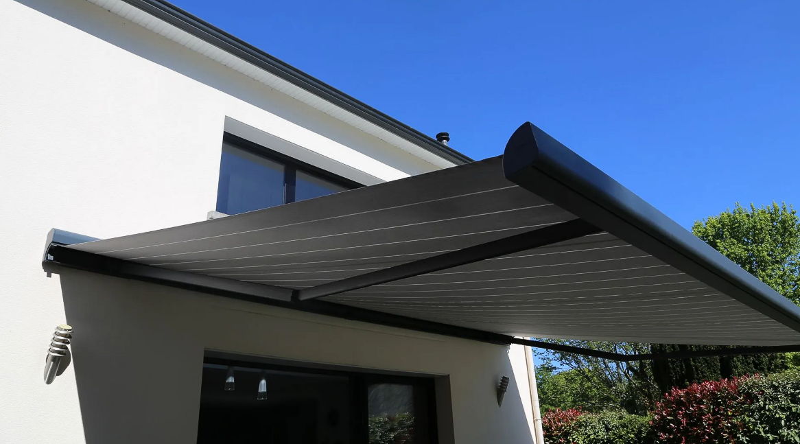 Extérieur de maison moderne avec un auvent rétractable noir déployé au-dessus d'une terrasse