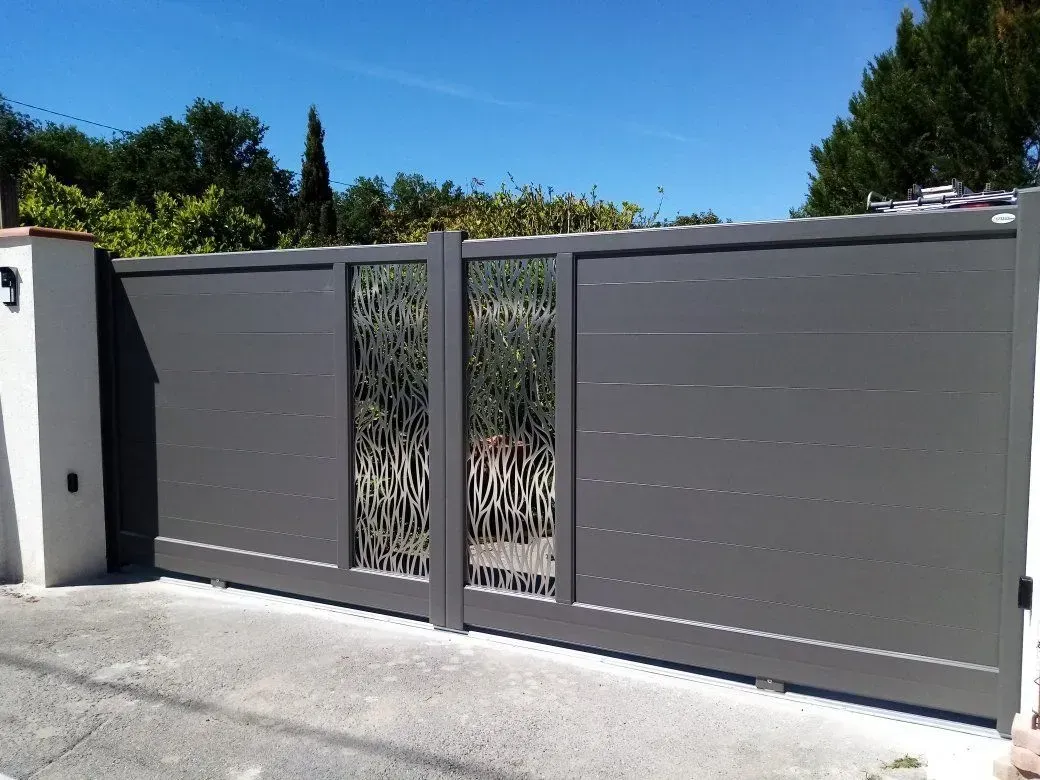 Portail d'allée moderne en métal gris avec un panneau central décoratif étroit et des poteaux muraux blancs sous un ciel bleu