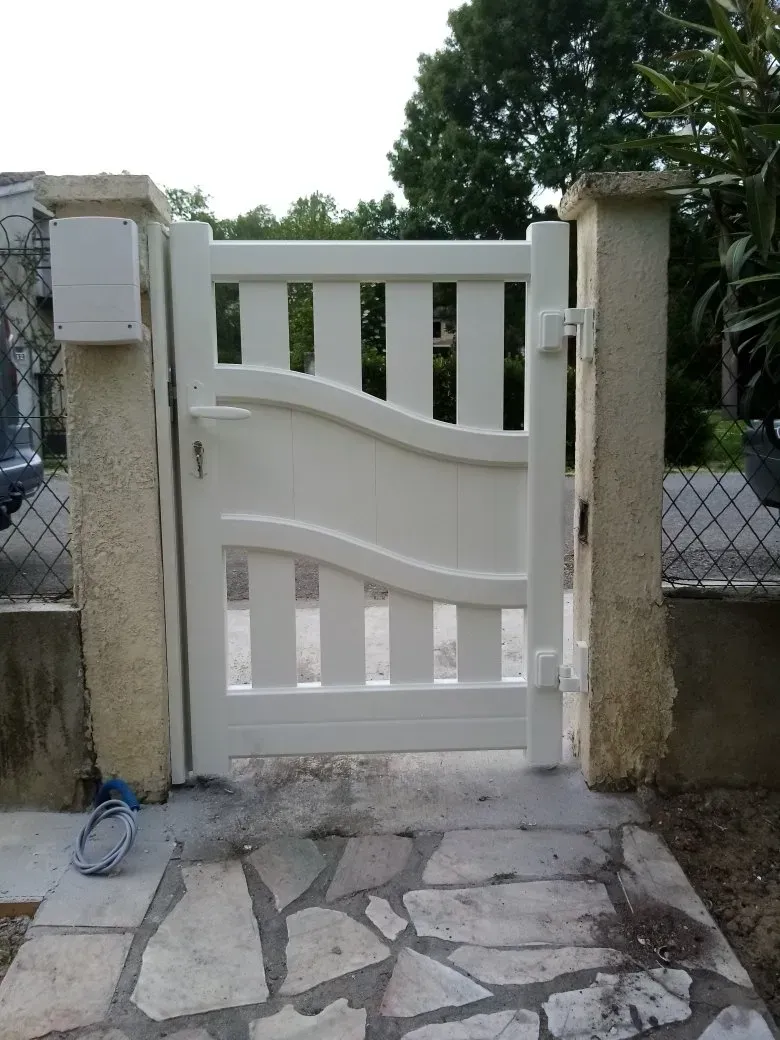 Portail blanc entre des piliers de pierre à l'entrée d'une cour, avec une allée de pierre devant.