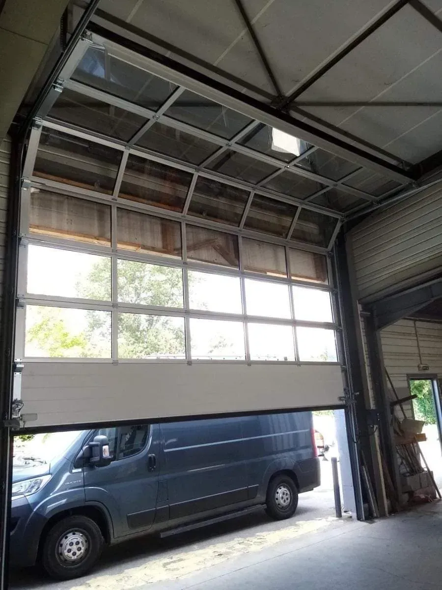 Fourgonnette bleue garée à l'intérieur d'un grand garage industriel, porte sectionnelle ouverte.