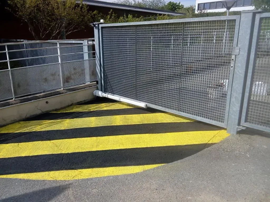 Rampe à rayures jaunes et noires à côté d'un portail et d'une clôture en grillage dans un espace extérieur ensoleillé