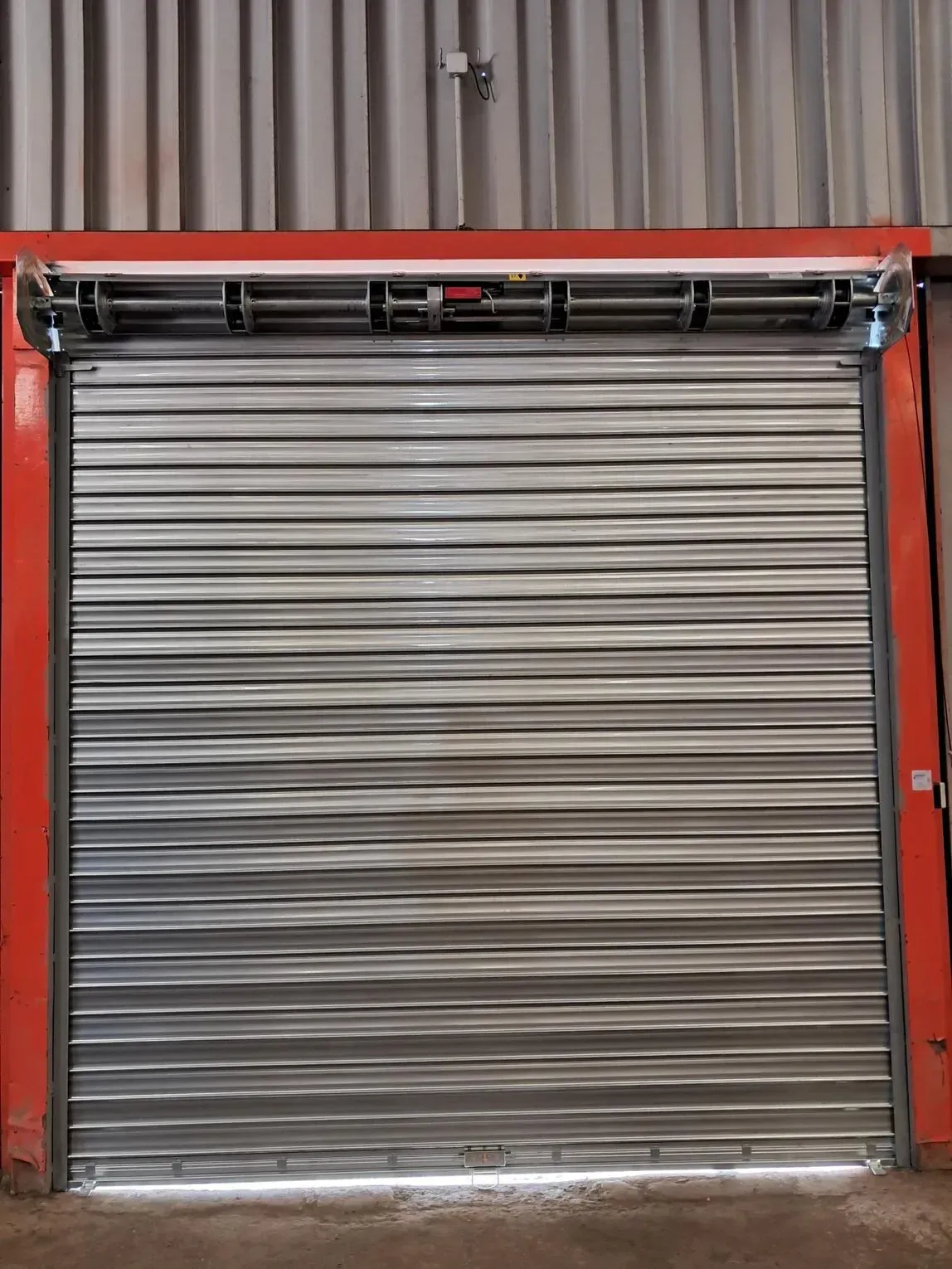 Porte sectionnelle métallique argentée fermée avec un cadre rouge devant un mur ondulé